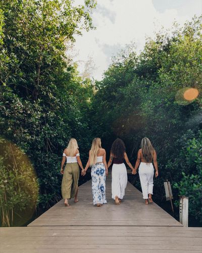 Vier Frauen gehen Hand in Hand über einen Holzsteg auf das Wasser zu, von hinten fotografiert
